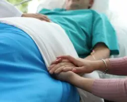 older woman laying in a bed with a younger woman holding her hand