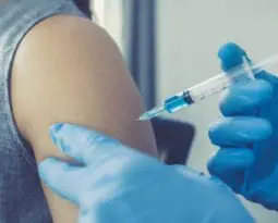 gloved hands injecting a vaccine into an exposed shoulder