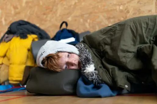 young ginger boy snuggled with green blankets laying down on a bag, facing the camera