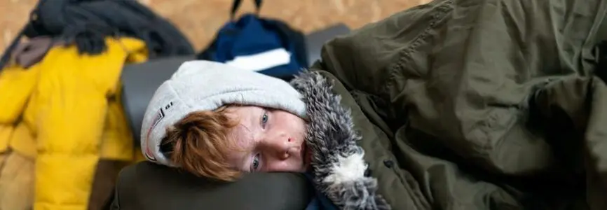 young ginger boy snuggled with green blankets laying down on a bag, facing the camera