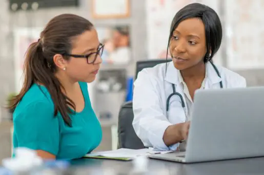 Female african american doctor talks to young hispanic patient while looking at computer