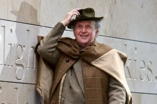 middle aged white man in brown layered clothes holding his wide brimmed hat