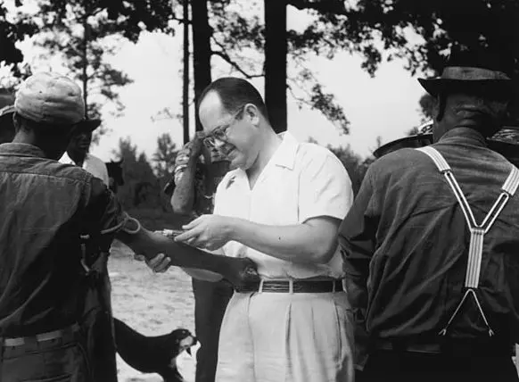 white man taking blood sample from black man's arm to test for Syphilis , part of the Tuskegee study.