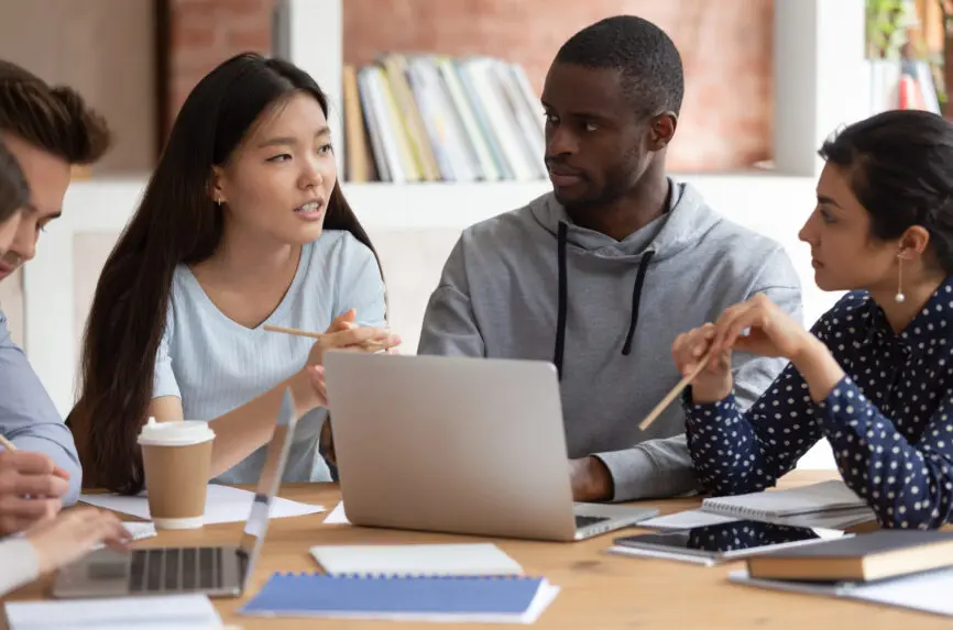 Focused young indian girl and black guy listening to groupmate. Asian female student explaining school project details or sharing ideas with college friends. Group of diverse teens working together.