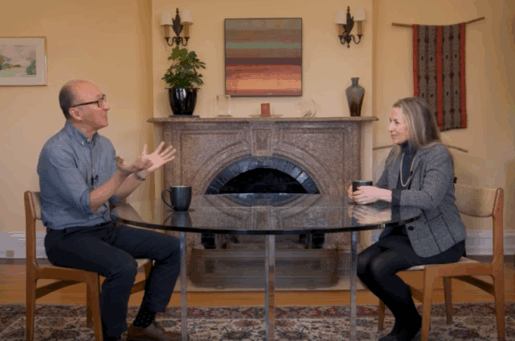 balding asian man with glasses talks to blond white woman around glass table