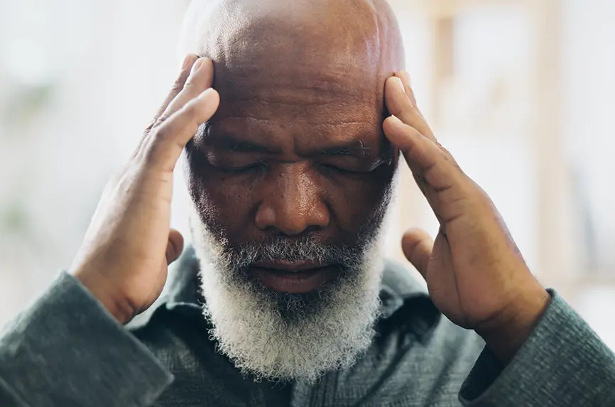 older man of color with white beard, holding his forehead