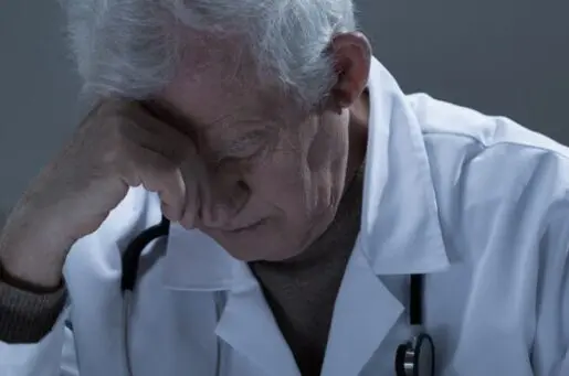 aged doctor with his head in his hand