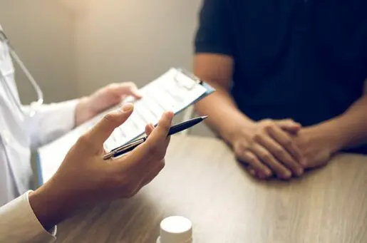 doctor holding prescription pad with pen in hand talking to a man in a blue shirt