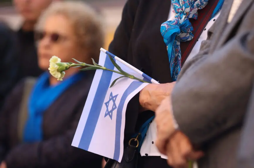 Details with the hands of a woman holding the Israeli flag and a flower during a ceremony commemorating the October 2023 attacks.
