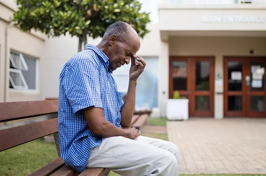 Sad senior man sitting on wooden bench outside nursing home