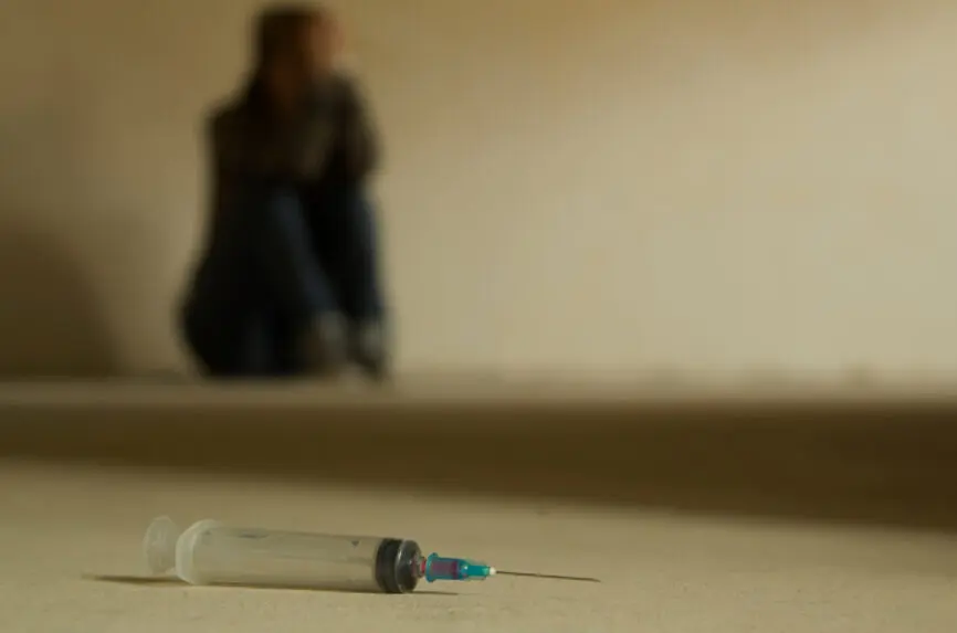 Drug addicted teen sitting on the floor background with syringe in foreground