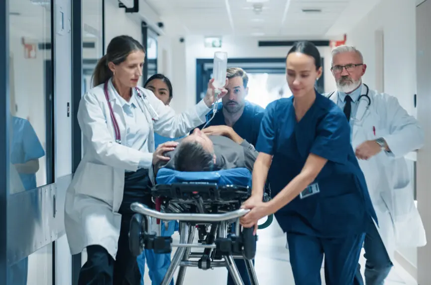 Diverse Emergency Medical Team Rushing Down a Hospital Corridor, Carefully Pushing a Stretcher with an Injured Patient. Nurses and Doctors Coordinate Urgent Life-Saving Efforts