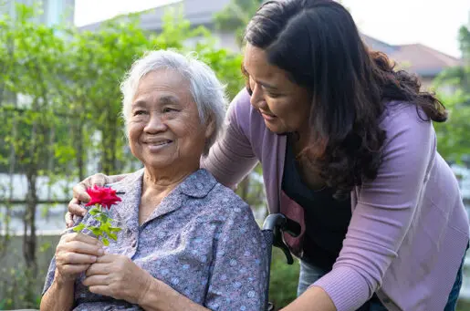 older asian woman in wheelchair, with young woman leaning over her, smiling