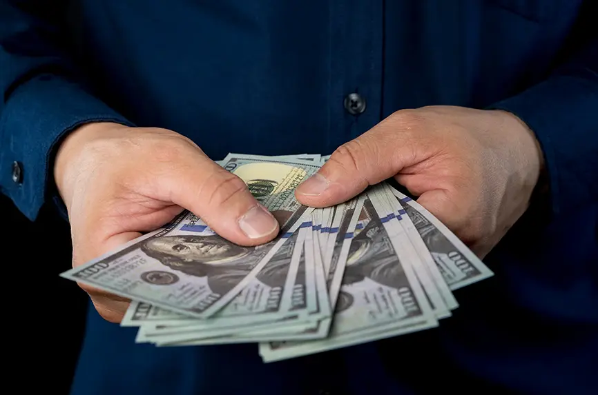 Big pile of money dollars in the hand. Close up of businessman counts money in hands. American Dollars Cash Money. 100 dollars banknotes in the background.