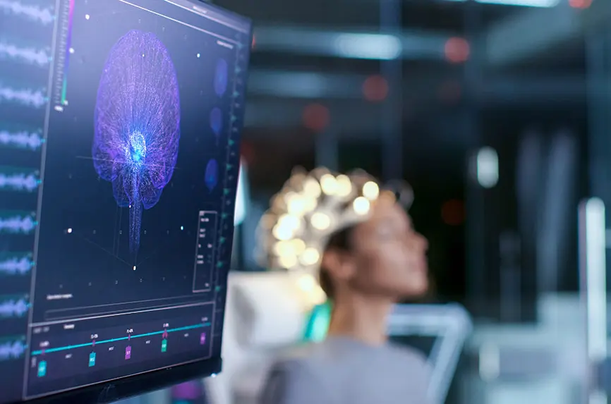 Woman Wearing Brainwave Scanning Headset Sits in a Chair In the Modern Brain Study Laboratory/ Neurological Research Center. Monitors Show EEG Reading and Brain Model.