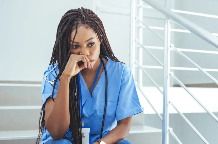 Shot of a young nurse looking stressed out while sitting at a window in a hospital. Mentally and physically exhausted. Close up of upset female nurse. Worried and stressed doctor sitting on corridor