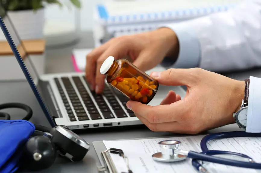 Male medicine doctor hands hold jar of pills and type something on laptop computer keyboard. Panacea and life save, prescribing treatment, legal drug store, take stock, consumption statistics concept