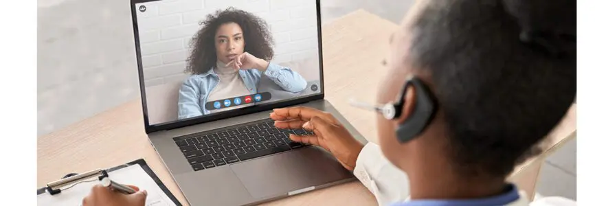 African doctor wear headset consult female black patient make online webcam video call on laptop screen. Telemedicine videoconference remote computer app virtual meeting. Over shoulder videocall view.
