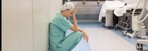 woman in scrubs leaning crouched against a wall