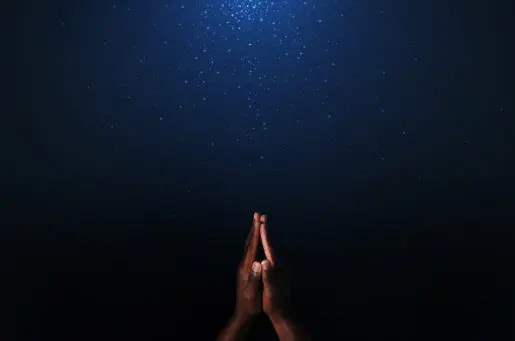 brown hands praying against a blue background