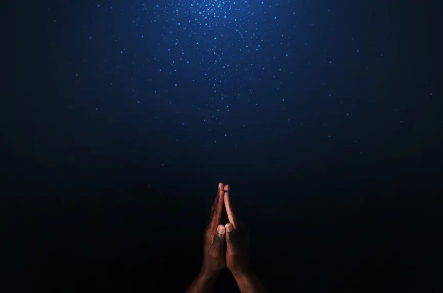 brown hands praying against a blue background