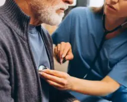 female nurse holding stethoscope to older man's heart