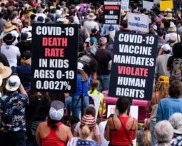 large crowd of protesters, one very large black sign stating "Covid-19 death rate in kids ages 0-10 is 0.0021%" in white lettering