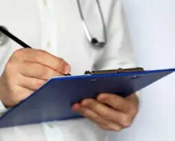 person in doctor's white coat writing on pad