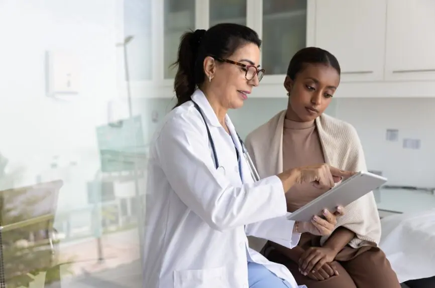 a young white woman doctor shows a young black woman patients a paper