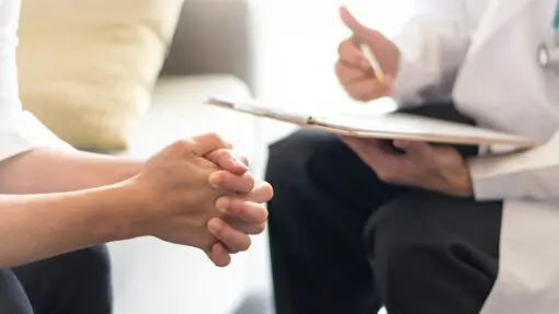 clasped hands of patient, doctor's hands with pen and clipboard