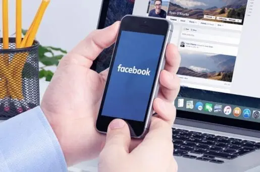 man holding an iPhone with the app Facebook open