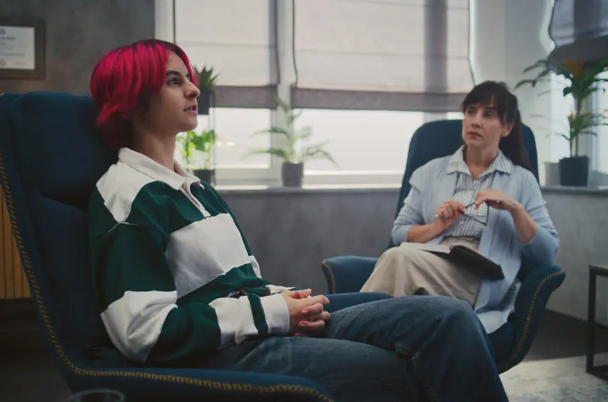 Girl and psychotherapist at therapy session looking for solutions to problems. Patient sitting in chair, looking up and sharing feelings. Therapist taking notes in notebook. Psychology. Slow Motion.