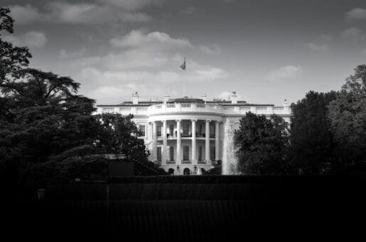 black and white image of the white house, a rounded pillared building behind collections of trees