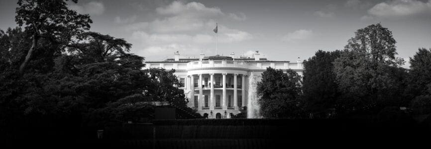 black and white image of the white house, a rounded pillared building behind collections of trees