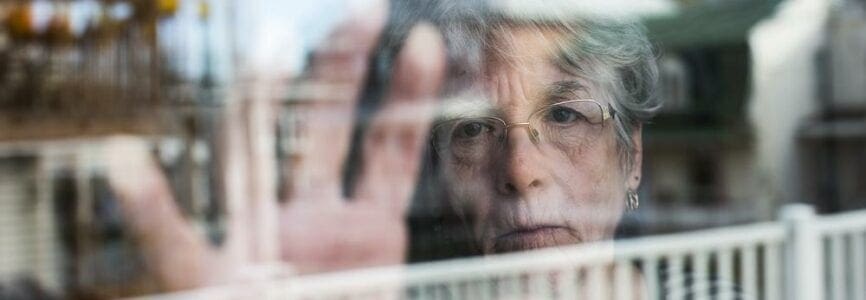 A Senior woman looking out through a window like depress