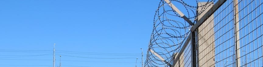 Barbed wire on the fence, concept for the protection of territory, property, military installations, the US and Mexico Border or places of detention, wide view against a blue sky.