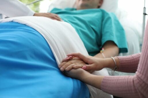 older woman laying in a bed with a younger woman holding her hand