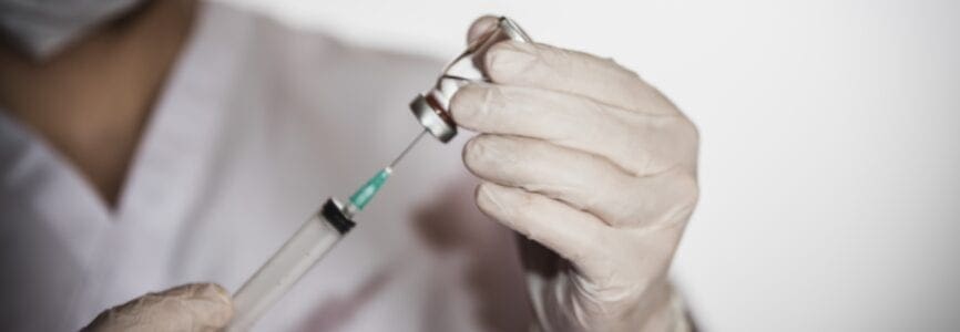 A health worker drawing vaccine in vial into syringe for COVID-19, measles, flu shots