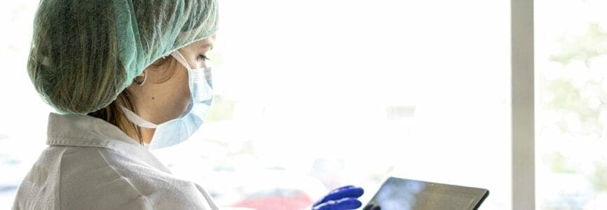 Cropped shot of an unrecognizable female nurse using a digital tablet while standing in a hospital. whit a mask