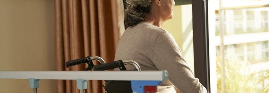 rear view of senior asian woman sitting in wheel chair in nusing home or hospital ward looking out of window