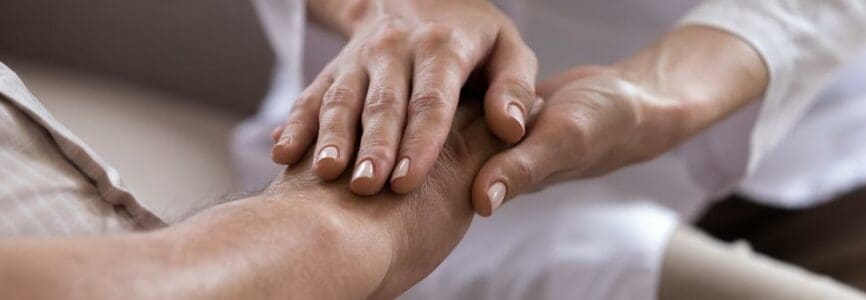 Close up of professional female caregiver hold senior male patient hands showing support and empathy at nursing home, caring doctor or nurse comfort support mature man, elderly healthcare concept