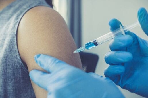 gloved hands injecting a vaccine into an exposed shoulder