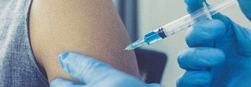 gloved hands injecting a vaccine into an exposed shoulder