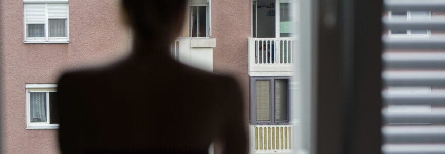 Home quarantine and social distancing during covid pandemic. Silhouette of lonley caucasian woman standing by window, anxiously looking out. Coronavirus infection, pandemics, disease outbreaks.