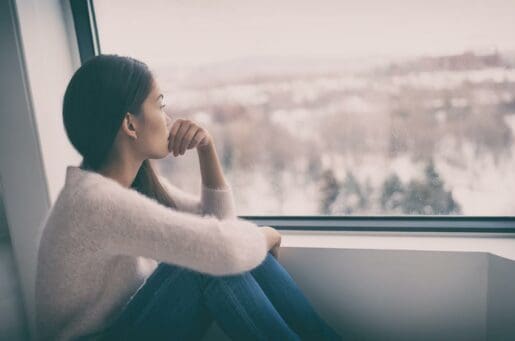 young woman, hair braided sitting in a window sill looking out over a city