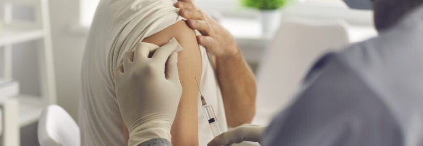 Immunization and disease prevention concept. Doctor giving antivirus injection to young man. Close-up patient in medical face mask getting flu or Covid-19 antiviral vaccine during vaccination campaign