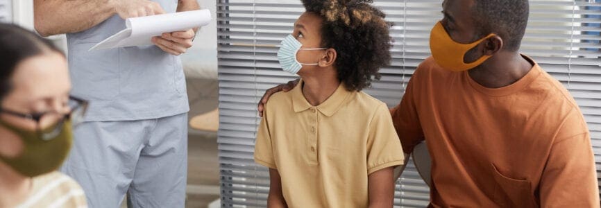 Portrait of African-American family wearing masks and looking at doctor while waiting in line at medical clinic