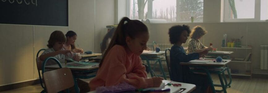 Diverse group of positive pupils sitting at desks at school class. Mixed race students doing class work at elementary school. Focused schoolboys and schoolgirls studying in school room