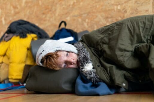 young ginger boy snuggled with green blankets laying down on a bag, facing the camera