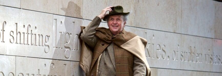 middle aged white man in brown layered clothes holding his wide brimmed hat